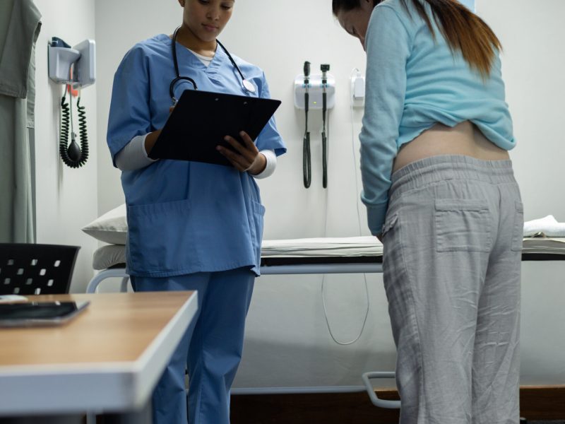 Front view of Caucasian female doctor weighing pregnant Caucasian woman in examination room at hospital