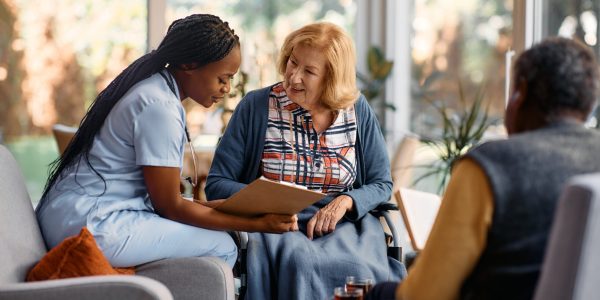 African American nurse analyzing senior woman's medical record while talking to her at nursing home.