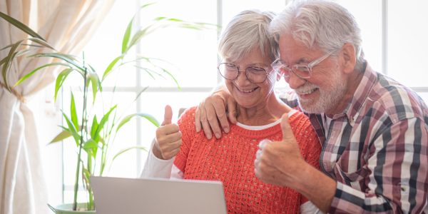 Portrait of cheerful senior couple video calling together on laptop expressing positivity and happiness. Joyful and beautiful senior couple sitting at home